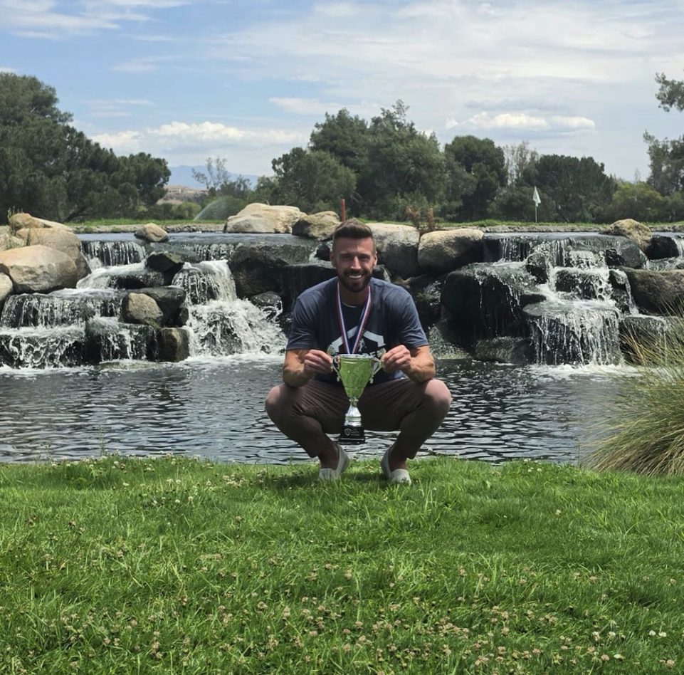 James Hardy crouching with the US Open trophy beside a waterfall at Temecula Creek